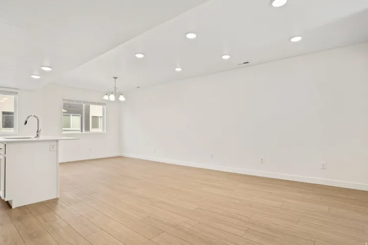 Open-concept living area featuring light wood-finish flooring, recessed ceiling lighting, and a modern chandelier