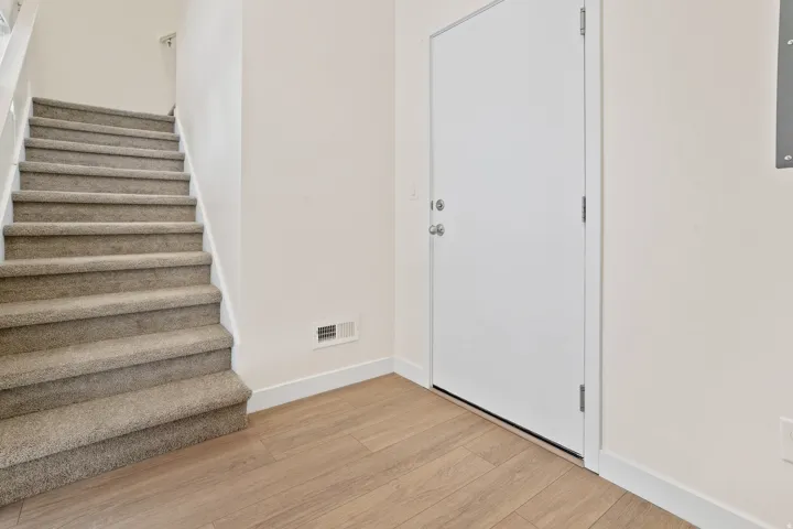 Entryway featuring wood-finish flooring, a white door, and a staircase with neutral-toned carpeting