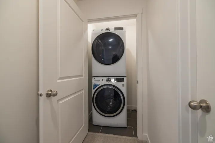 Dedicated laundry closet featuring a stacked washer and dryer, finished with dark tile flooring
