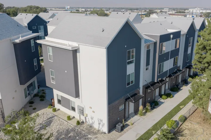 Modern row of townhomes featuring contrasting dark and light exterior siding, white window frames, individual covered entryways, and a concrete sidewalk with manicured grass borders