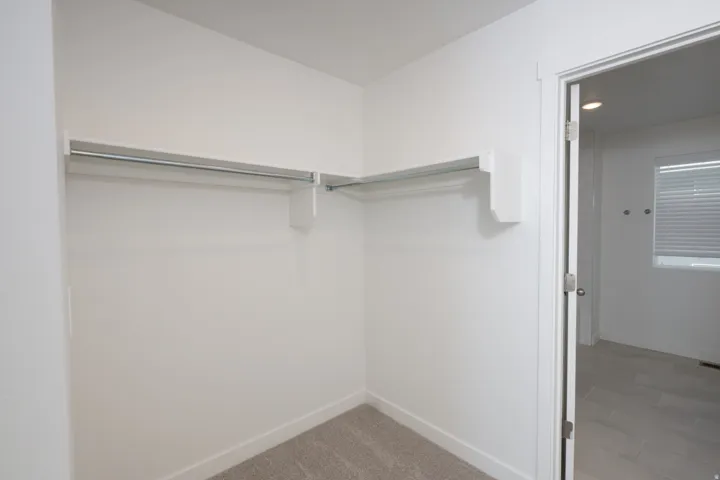 Spacious walk-in closet featuring dual hanging rods with substantial storage capacity, neutral carpet flooring, and clean white walls providing an organized dressing area