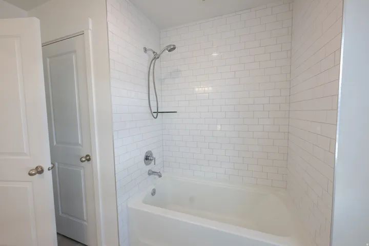 White subway tile shower surround with a built-in shelf, chrome fixtures, and a white bathtub