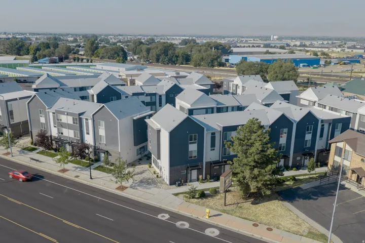 Modern multi-unit development featuring a mix of gray and dark blue facades, contemporary architectural lines, multiple gabled roofs, and manicured landscaping