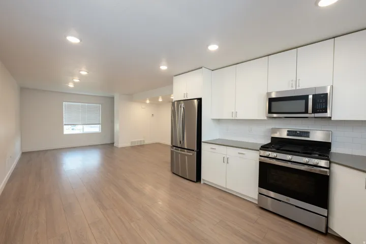 Open-concept kitchen and living area featuring wood-finish flooring, recessed lighting, and a window with blinds