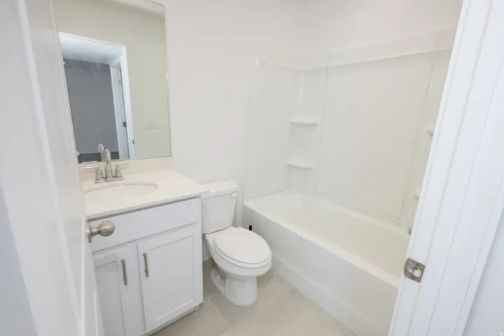 Bright bathroom featuring a white vanity with an undermount sink, a large wall mirror, and a white bathtub with a built-in shower surround