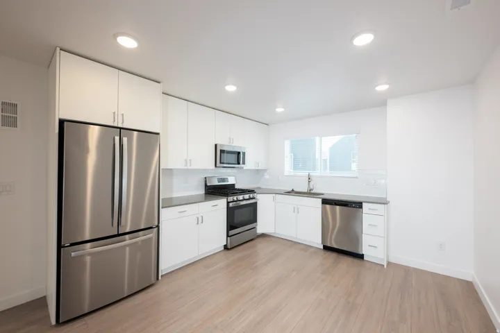 Modern kitchen featuring stainless steel appliances, white cabinetry, neutral countertops, a subway tile backsplash, and wood-finish flooring
