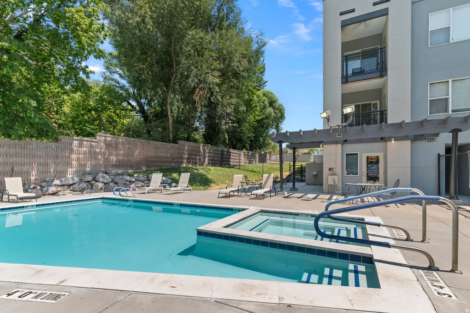Outdoor swimming pool with integrated hot tub, concrete deck, and a shaded pergola structure