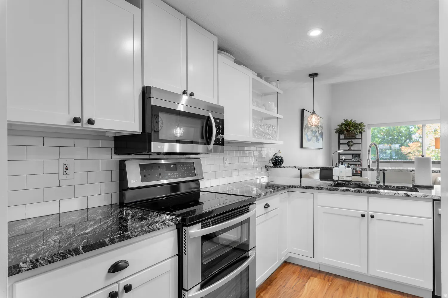 Modern kitchen featuring white shaker cabinetry, stainless steel appliances, dark stone countertops, a white subway tile backsplash, and wood-finish flooring