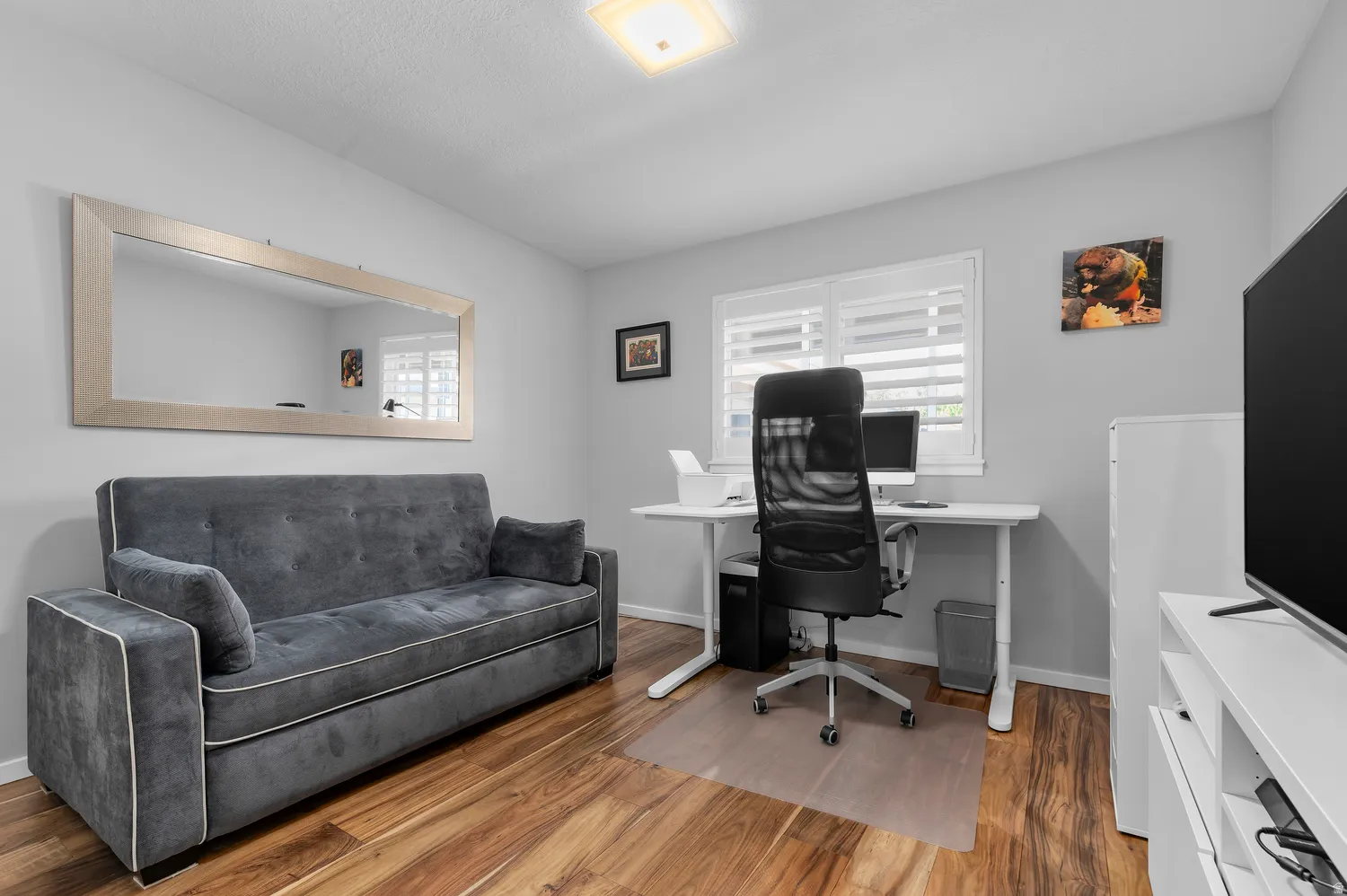 Room featuring wood-finish flooring, a window with plantation shutters, a light gray wall color, and a built-in overhead light fixture