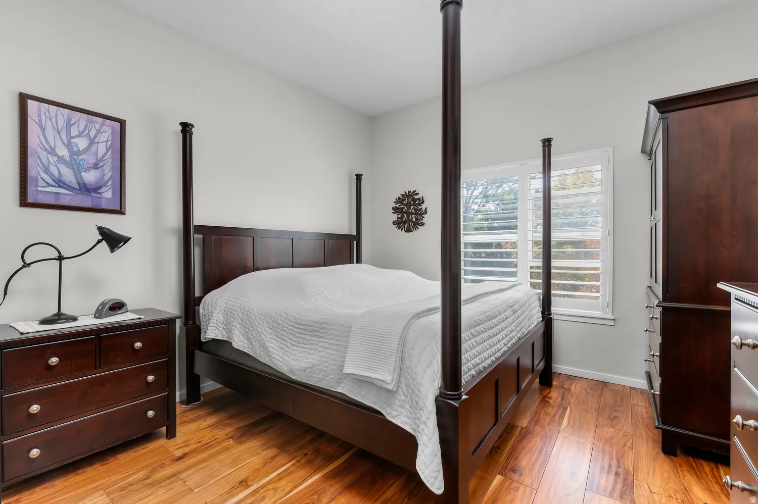 Bedroom featuring wood-finish flooring, light gray walls, and a window with white plantation shutters