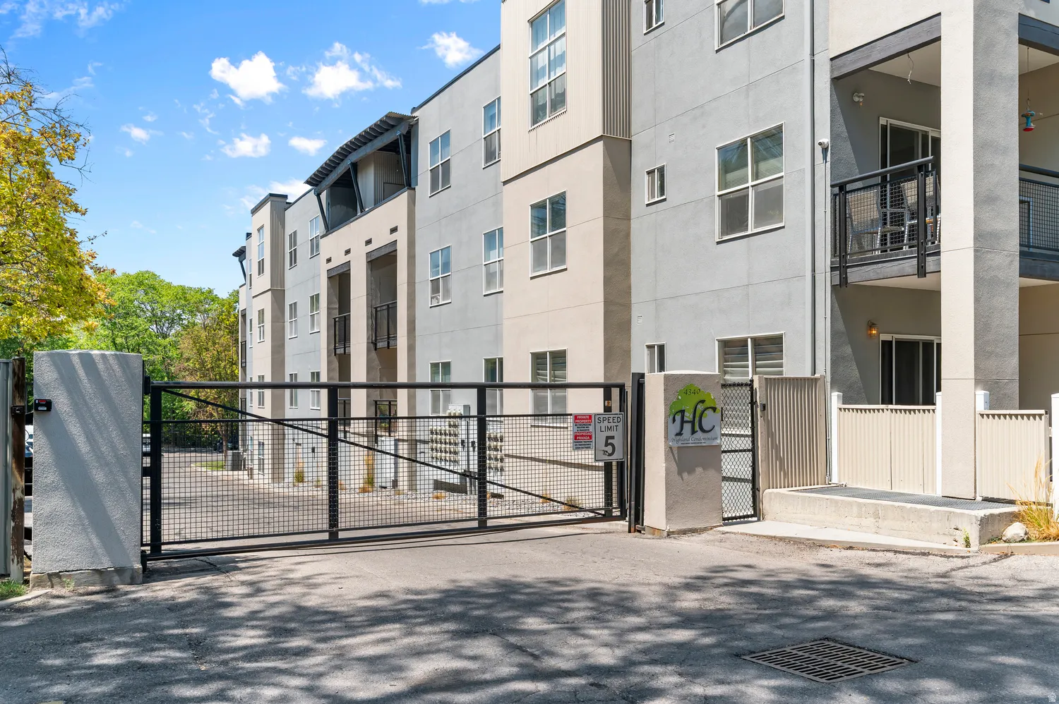 Gated entry to a modern multi-story building featuring balconies and a combination of smooth and textured exterior finishes