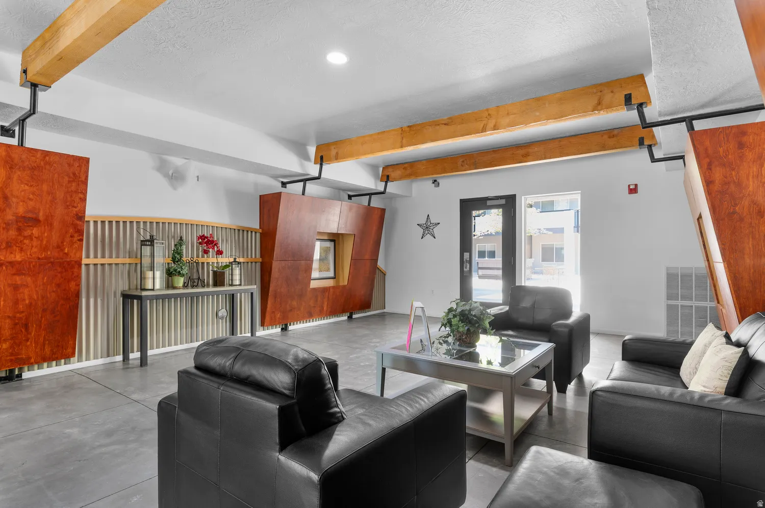 Lobby area featuring exposed wooden beams, concrete flooring, and an entrance door with a transom window