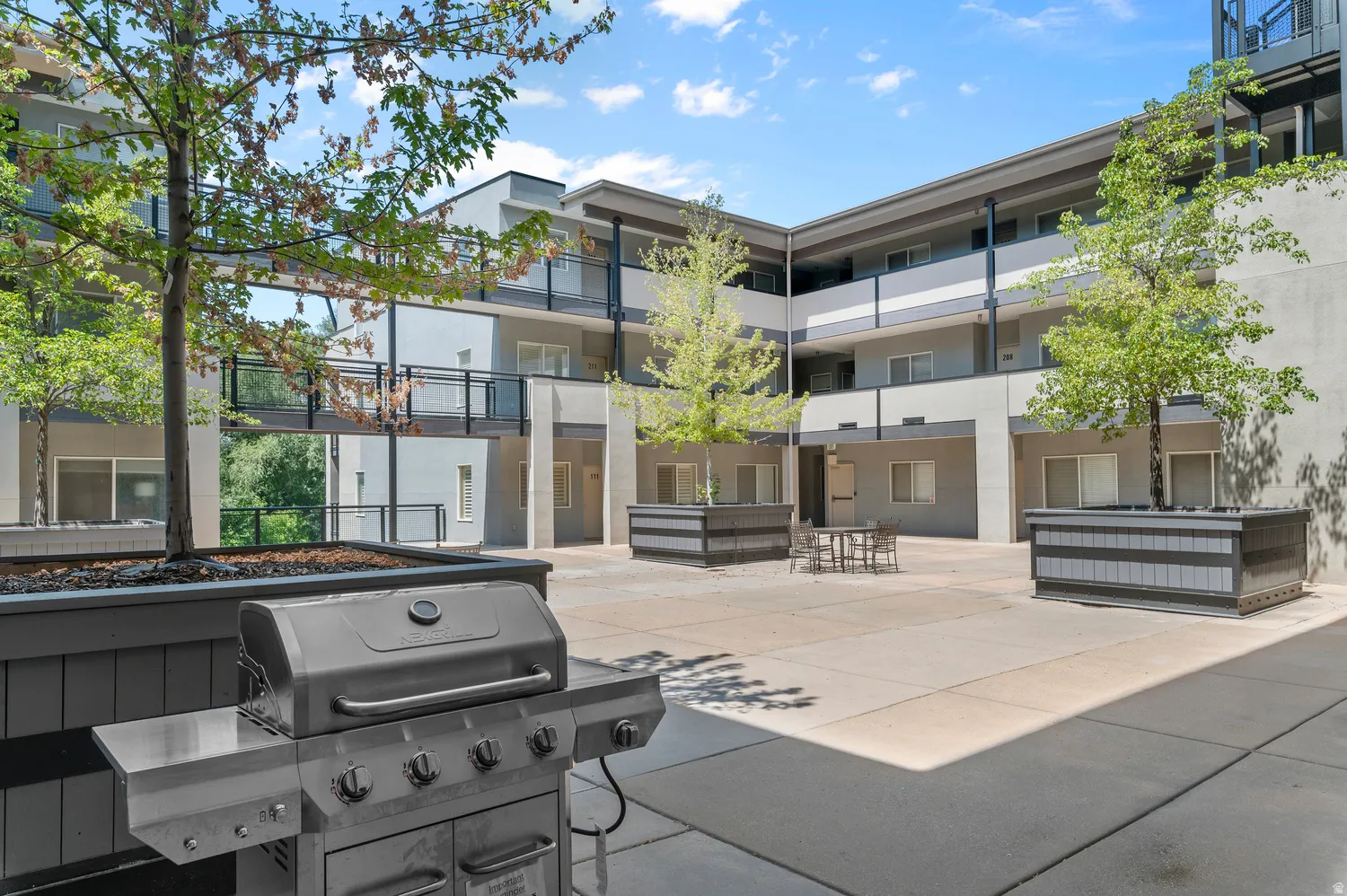 Courtyard featuring a gas grill, concrete paving, and planter boxes with mature trees
