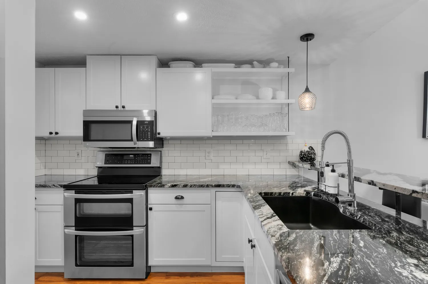 Kitchen featuring white cabinetry, subway tile backsplash, stainless steel appliances, dark stone countertops, and a black undermount sink with a gooseneck faucet