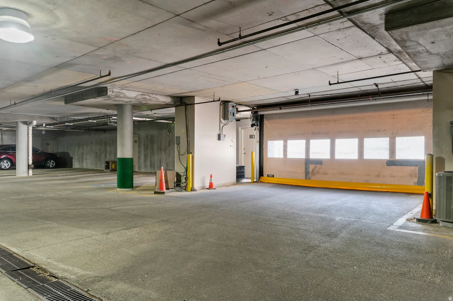 Secure underground parking facility featuring concrete flooring and ceiling, fluorescent overhead lighting, and a roll-up access door with multiple window panels