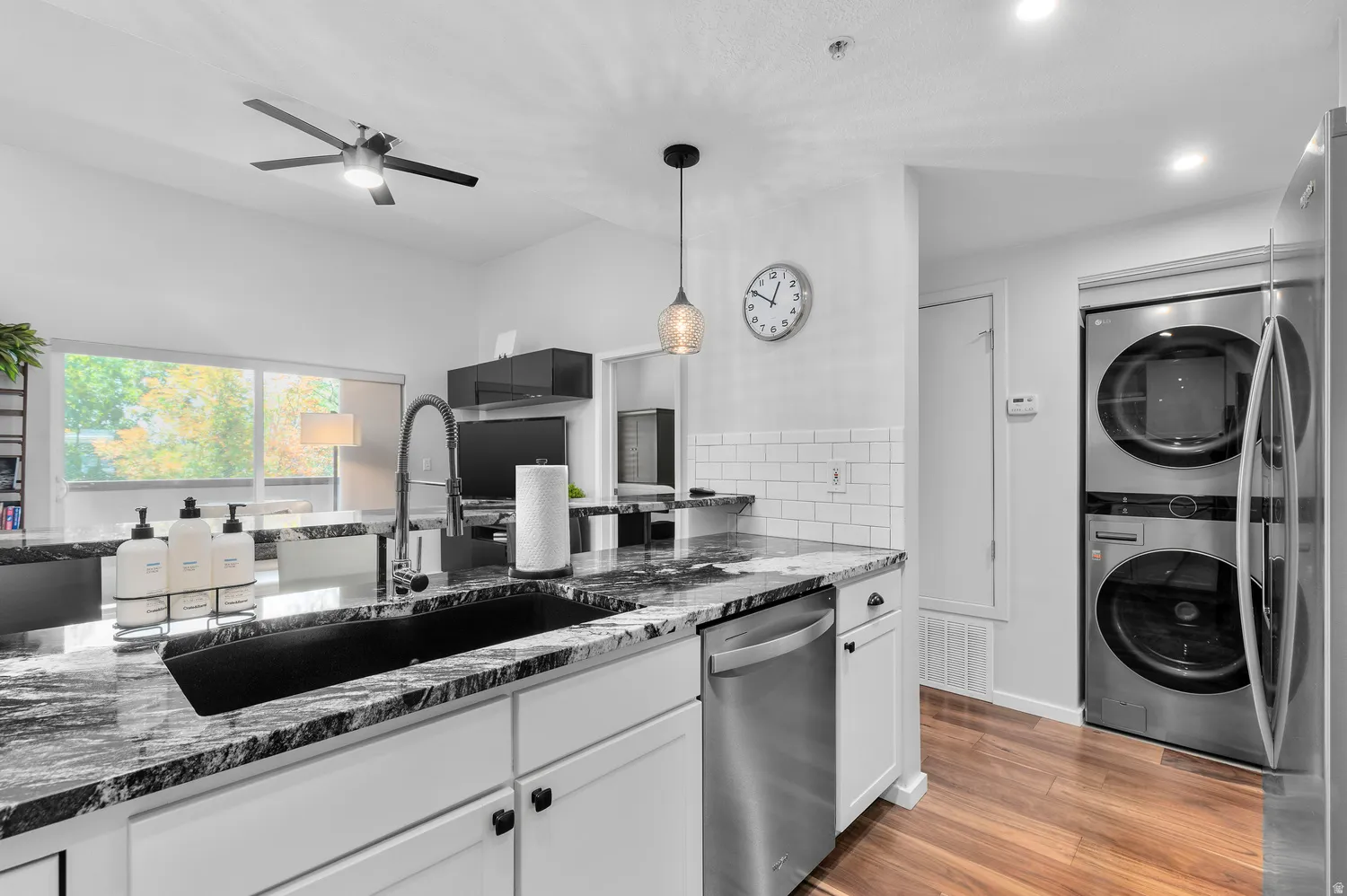 Modern kitchen featuring white cabinetry with black hardware, a striking black and gray veined countertop with waterfall edge, stainless steel appliances including a gas range and under-counter microwave, and a deep black undermount sink with contemporary