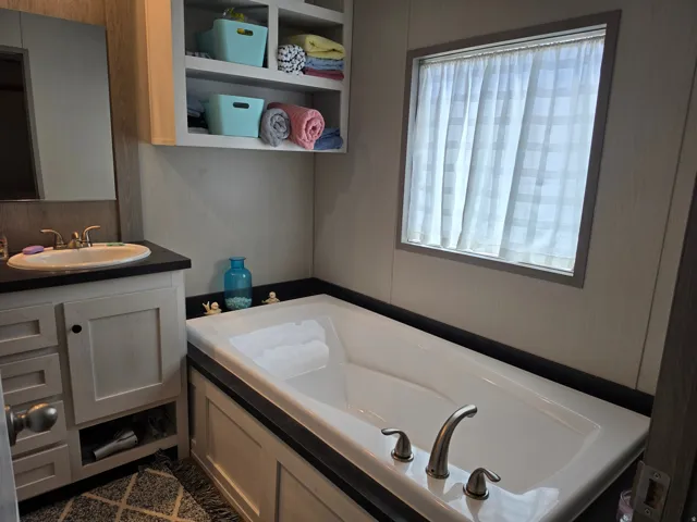 Spacious soaking tub with brushed nickel fixtures, complemented by an overhead storage cabinet, a vanity with under-sink storage, and a framed mirror
