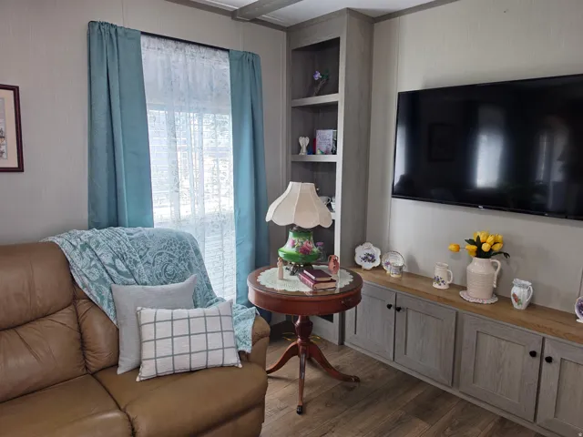 Living area featuring wood-finish flooring, a built-in media console with storage, open shelving, and eyebrow windows.