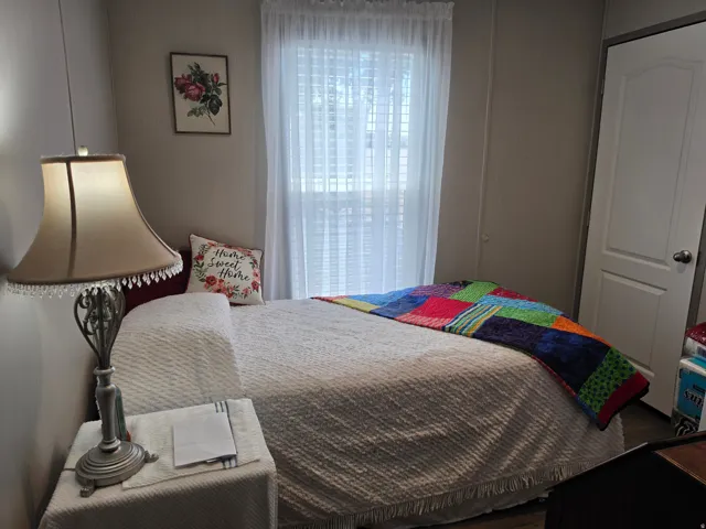 Bedroom 3. Light-filled room featuring a window with white sheer curtains, neutral wall paint, and a white interior door with a silver-tone knob