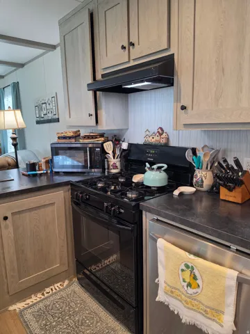 Kitchen featuring black appliances, wood-finish cabinetry, dark countertops, and wood-finish flooring
