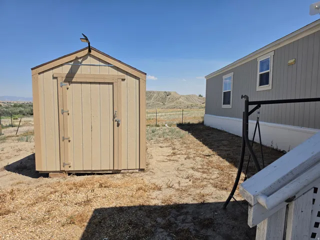 Detached storage shed with a gabled roof and light-colored siding, featuring a single entry door with visible hardware