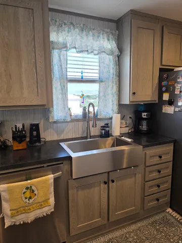 Kitchen featuring a large stainless steel farmhouse sink with a gooseneck faucet, dark countertops, and wood-finish cabinetry