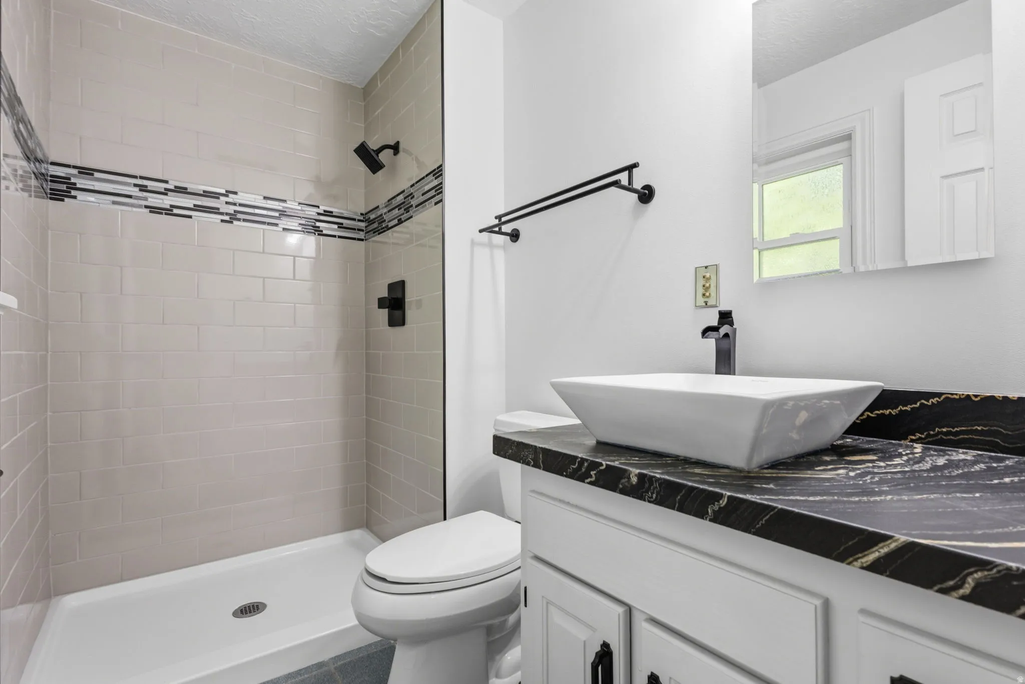 Primary bathroom featuring a walk-in shower with new tile and decorative accent band