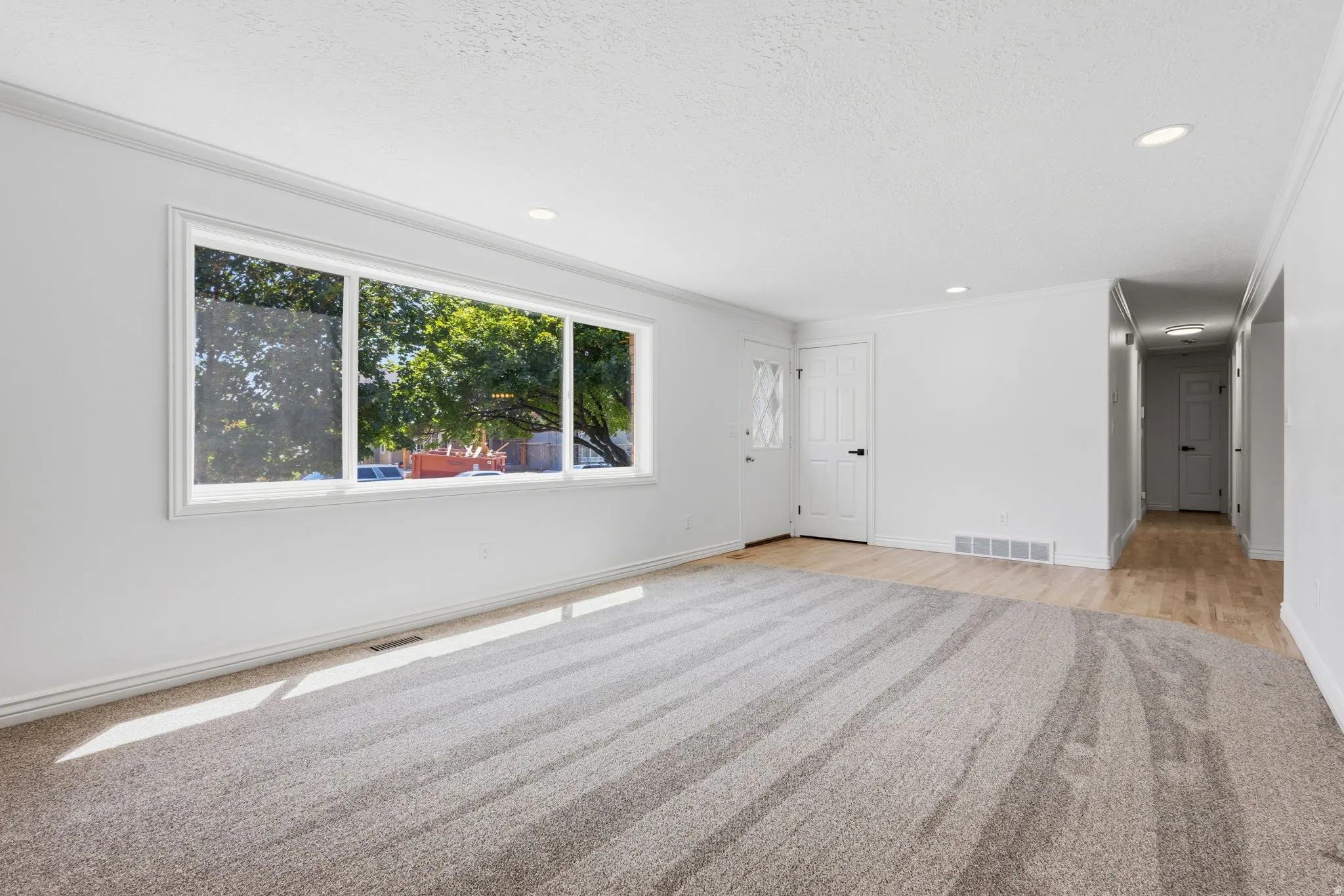Spacious living area featuring a large picture window, recessed lighting, gas fireplace, and a blend of carpet and hardwood flooring