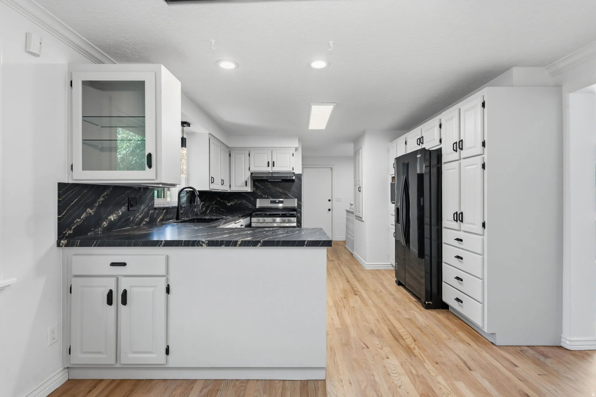 Fully updated kitchen featuring granite countertops and backsplash, refinished cabinets with new hardware, brand new stainless steel appliances, and hardwood flooring