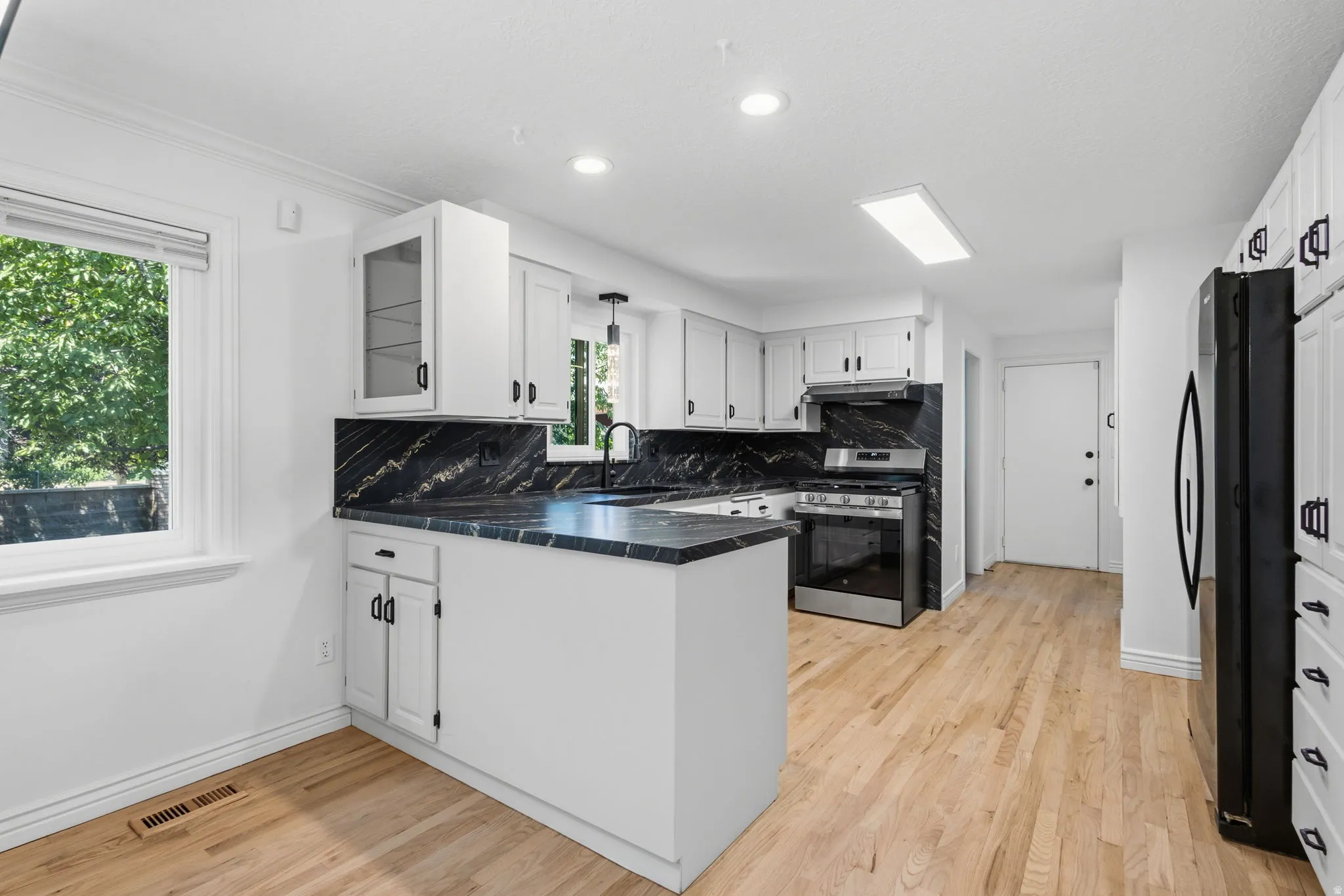 Fully updated kitchen featuring granite countertops and backsplash, refinished cabinets with new hardware, brand new stainless steel appliances, and hardwood flooring