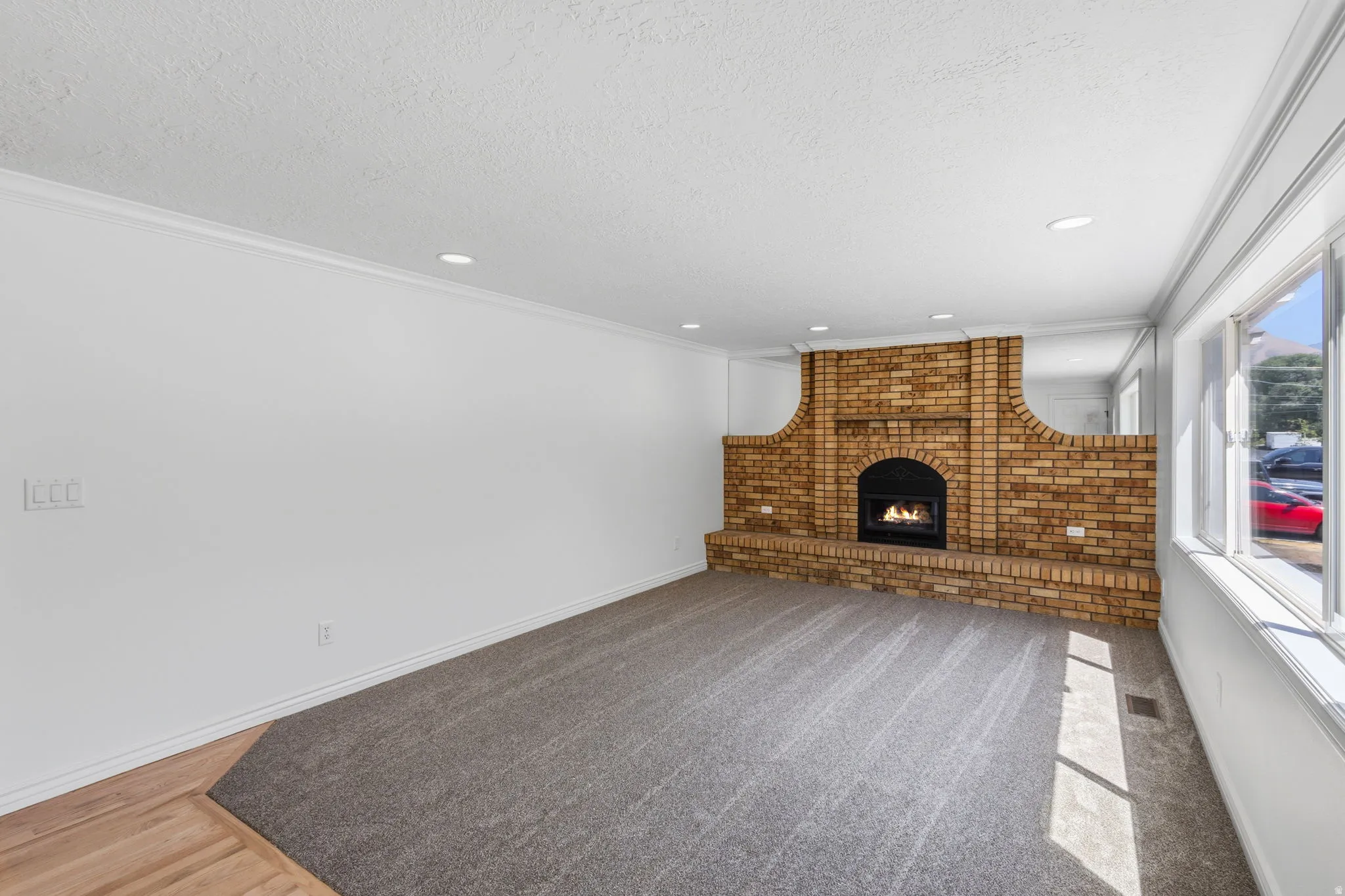Spacious room featuring a custom brick gas fireplace, new carpet, and new lighting