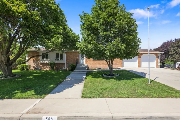 Brick and siding exterior featuring mature trees, a manicured lawn, a concrete walkway, and a two-car extra-deep garage