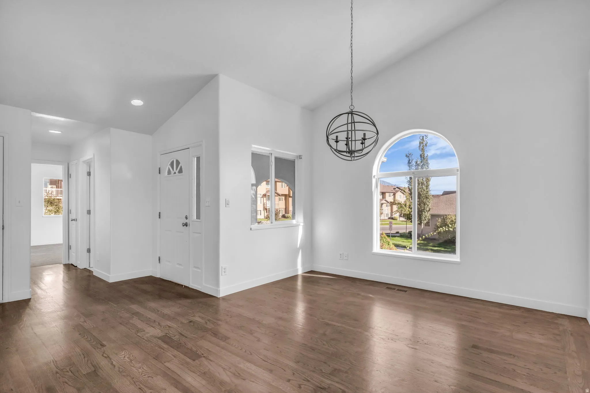 Vaulted ceiling with an orb chandelier, wood-finish flooring, arched window, and a white front door with decorative lites