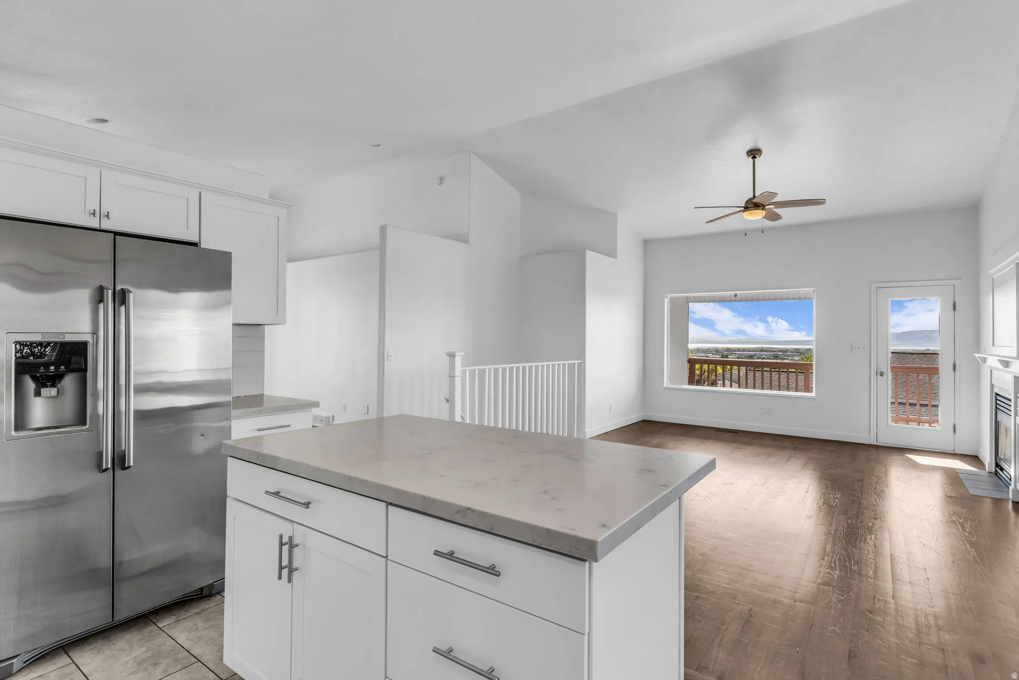 Stainless steel refrigerator, white cabinetry, island with a light-toned countertop, wood-finish flooring, and a ceiling fan