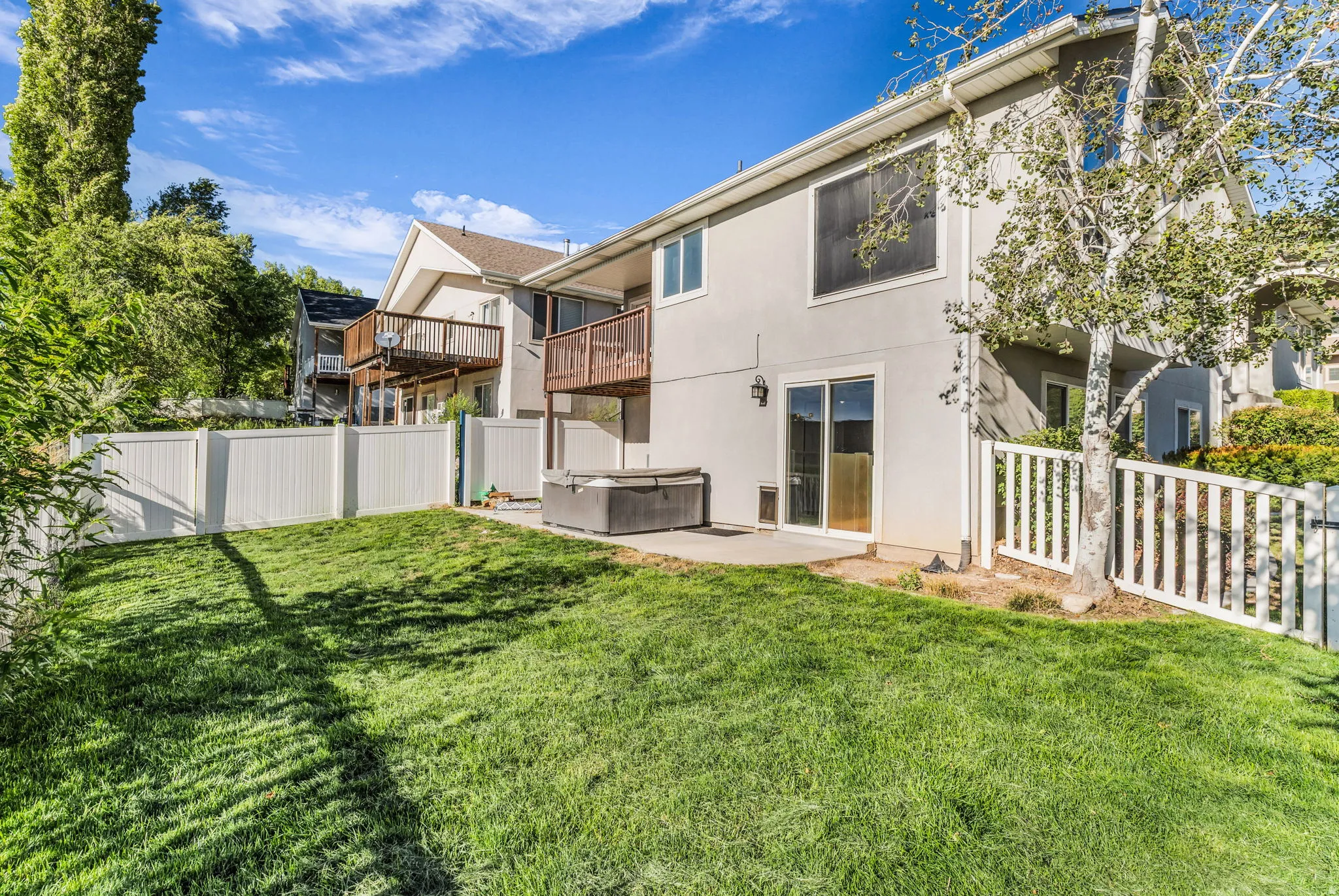 Expansive grassy yard with white privacy fencing, a concrete patio, and a sliding glass door entry