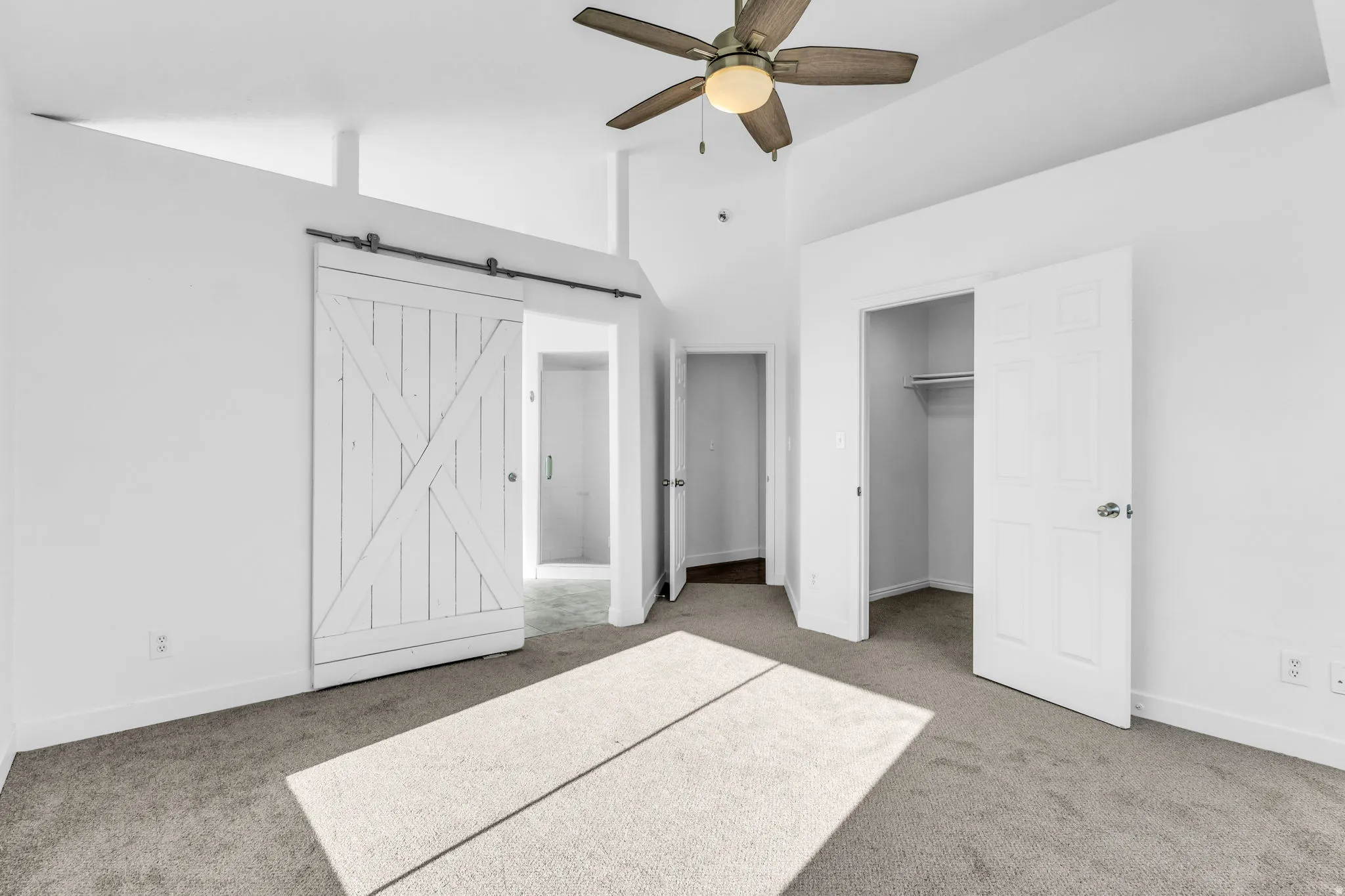 Primary Bedroom with Vaulted ceilings with a ceiling fan, white barn door, and carpet flooring