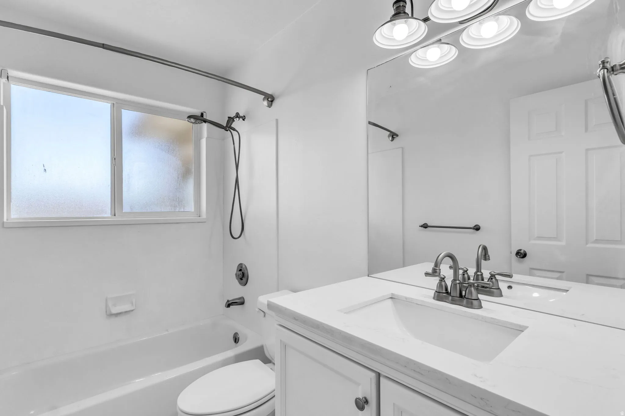 White vanity with an integrated sink, brushed nickel faucet, large wall mirror, and a multi-bulb vanity light fixture