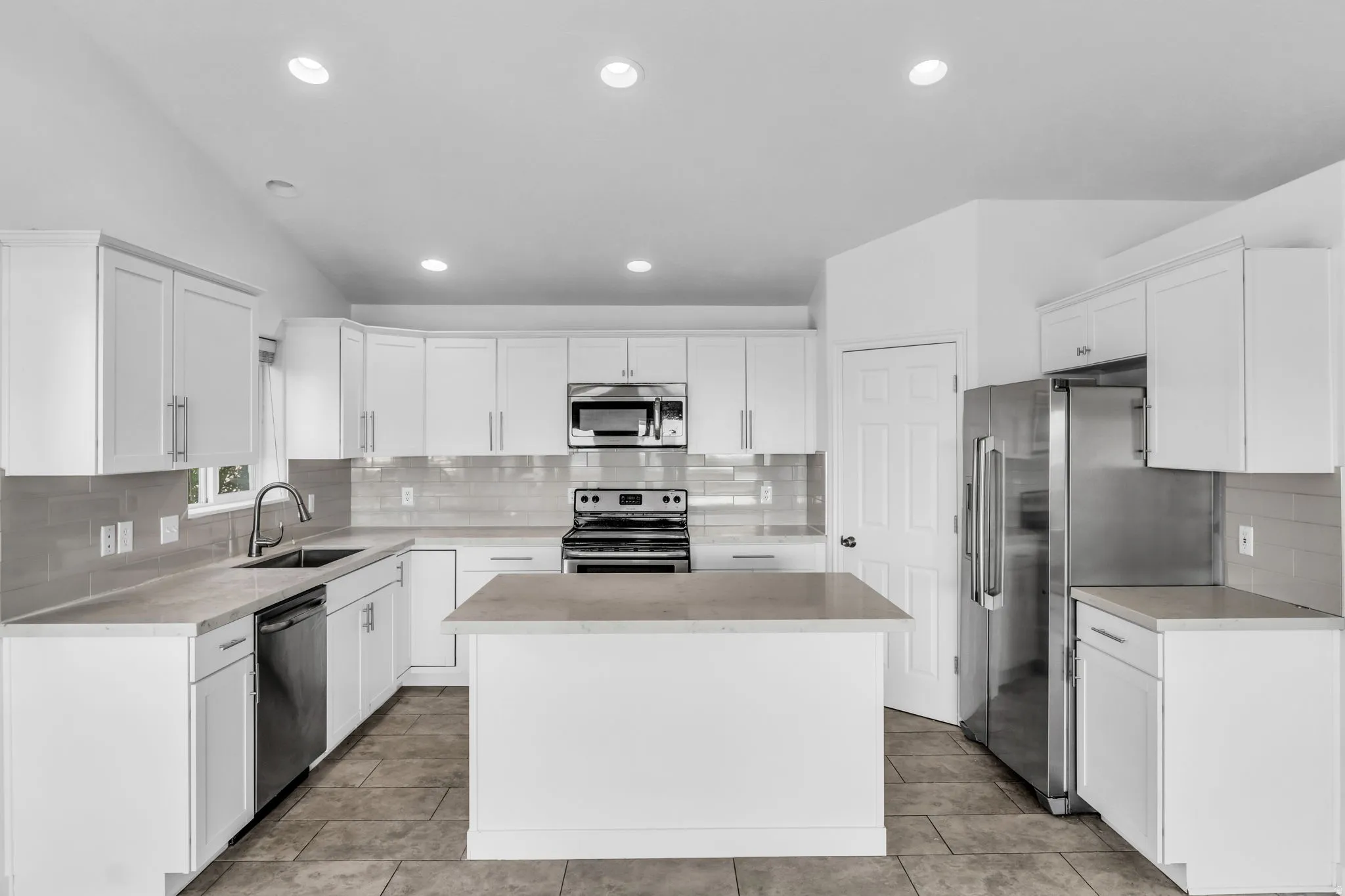 Kitchen featuring white cabinetry, stainless steel appliances, a center island, light-colored countertops, and tiled flooring