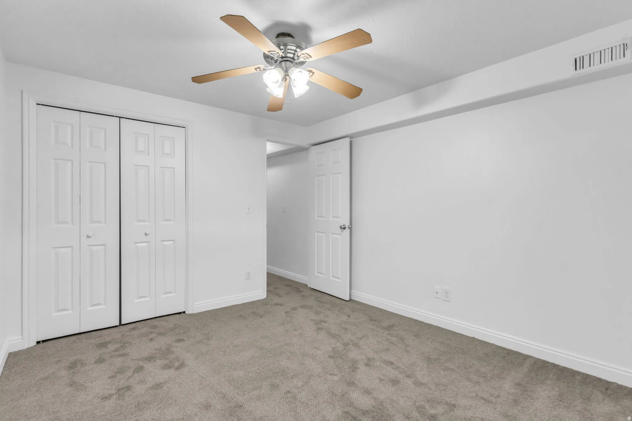 Textured new carpeting, bi-fold closet doors, ceiling fan with light fixture, and white painted walls