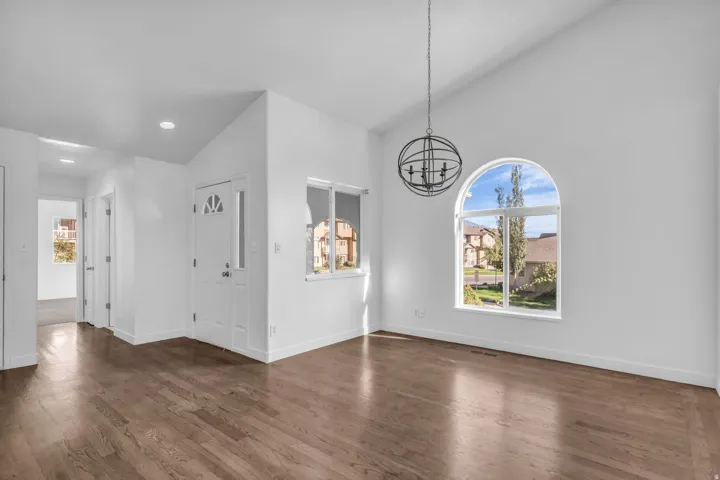 Vaulted ceiling with an orb chandelier, wood-finish flooring, arched window, and a white front door with decorative lites