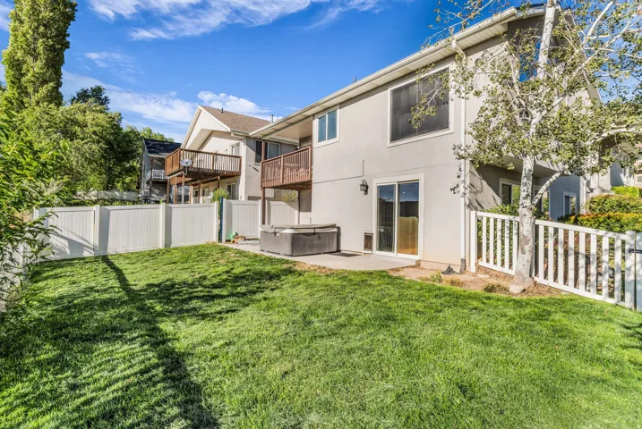 Expansive grassy yard with white privacy fencing, a concrete patio, and a sliding glass door entry