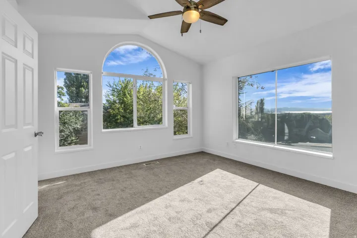 Primary Bedroom with Vaulted ceilings with a ceiling fan, arched window, multiple large windows, and carpet flooring
