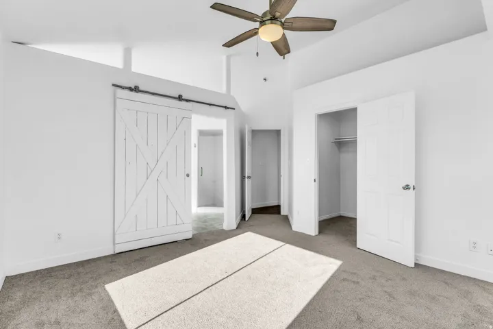 Primary Bedroom with Vaulted ceilings with a ceiling fan, white barn door, and carpet flooring