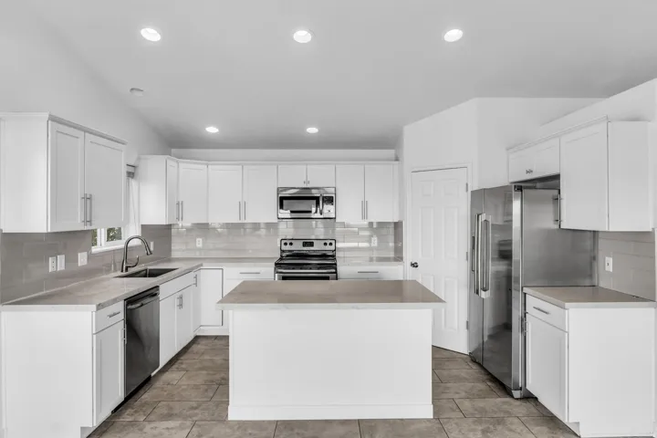 Kitchen featuring white cabinetry, stainless steel appliances, a center island, light-colored countertops, and tiled flooring