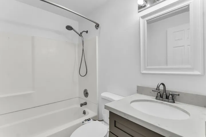 Bathroom featuring a shower-tub combination with a handheld showerhead, vanity with a light-colored countertop, and a framed mirror