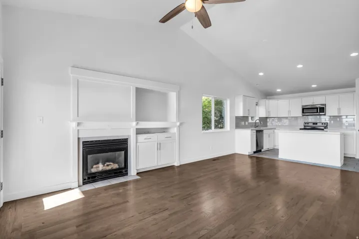 Vaulted ceilings, wood-finish flooring, built-in fireplace with surround, white shaker cabinetry, and stainless steel appliances