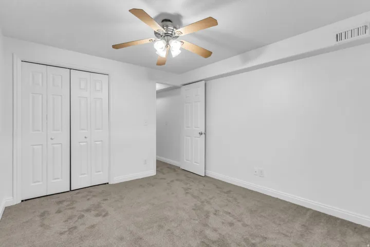 Textured new carpeting, bi-fold closet doors, ceiling fan with light fixture, and white painted walls