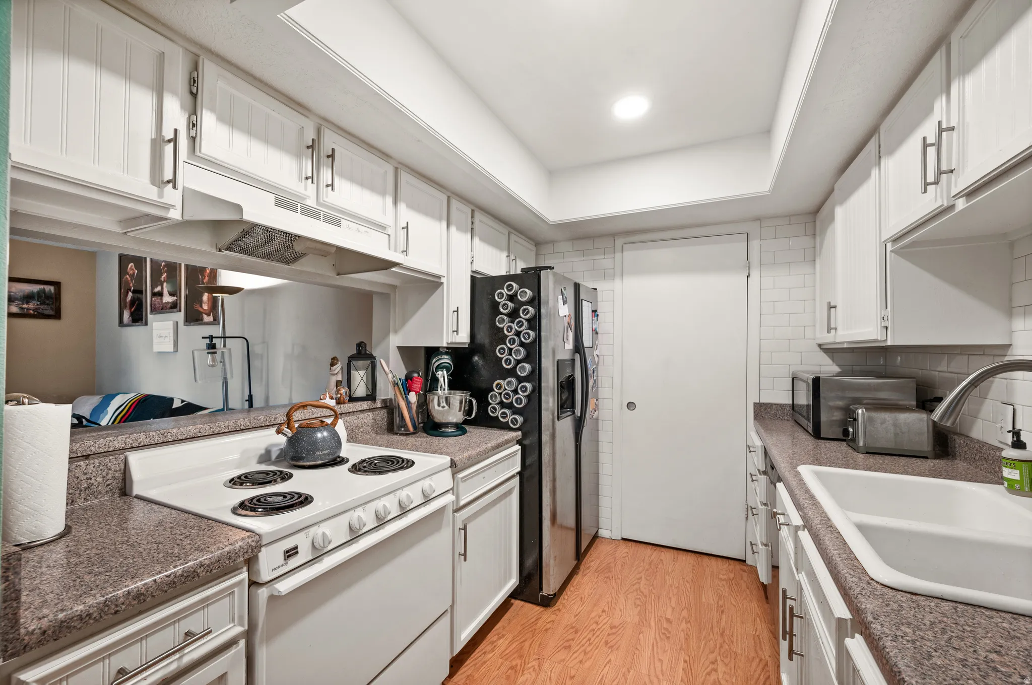 Kitchen featuring white shaker-style cabinetry, wood-finish flooring, and a subway tile backsplash