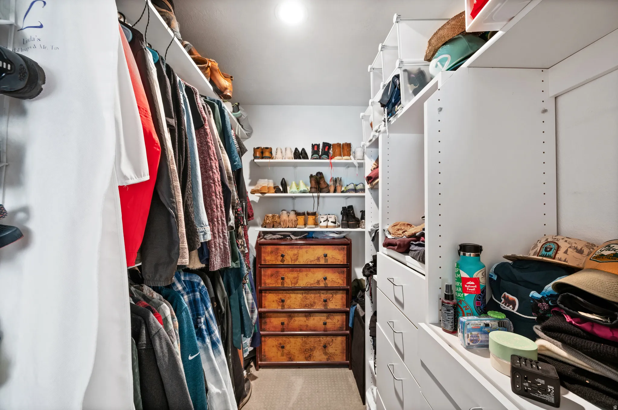 Walk-in closet featuring built-in white shelving, hanging rods, and a central chest of drawers with decorative pulls