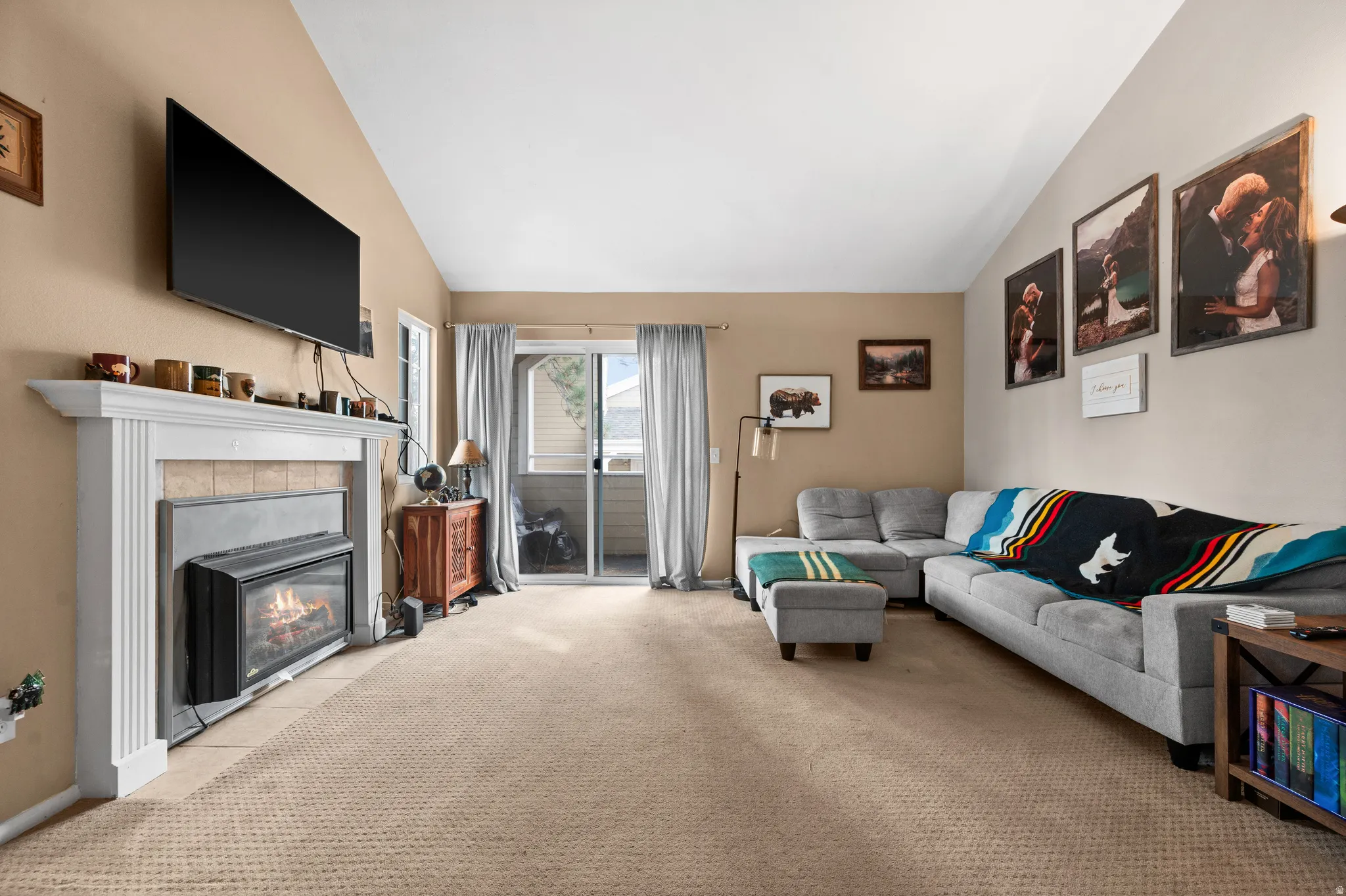 Living area featuring a fireplace with a white mantel, sliding glass doors, vaulted ceilings, and neutral-toned wall-to-wall carpeting